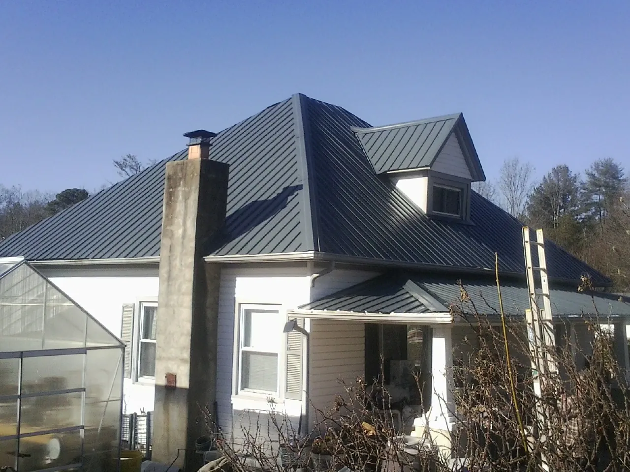 Dark blue standing seam metal roof on a white farmhouse with dormer — Slate & Tile Roof Repair by Roofing Brothers in Ladoga