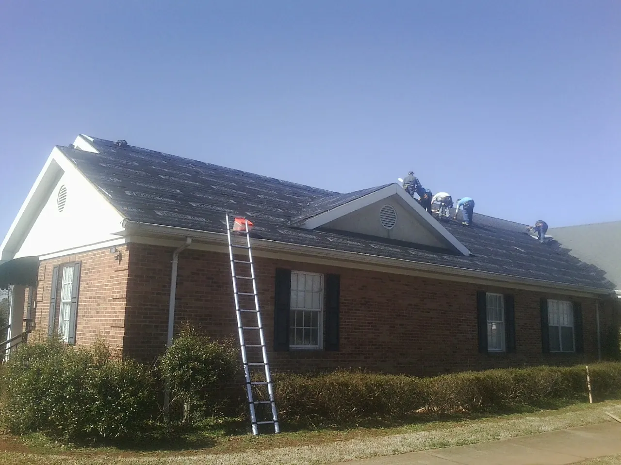 Crew tearing shingles off a brick ranch roof with a ladder set — Metal Roof Repair work by our crew in Ladoga