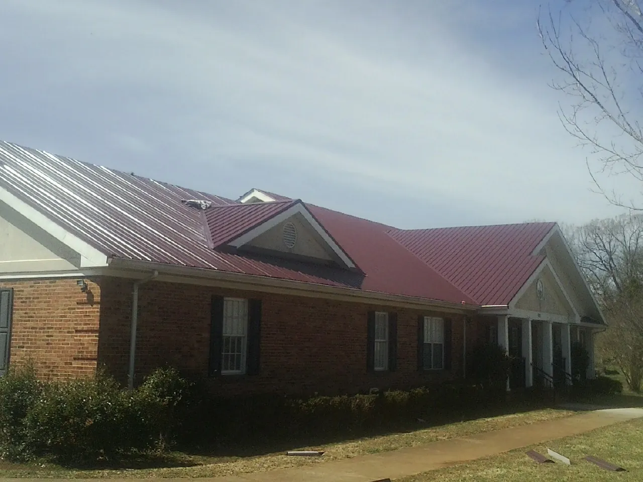 Red metal roof with gabled entries on a long brick building, from a Hail Damage Roof Repair job in Ladoga