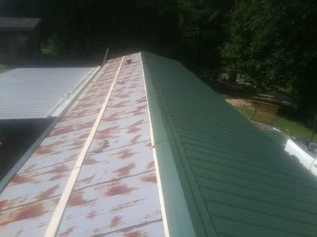 Old rusted panels beside newly installed green metal roofing — Wind Damage Roof Repair by Roofing Brothers in Ladoga