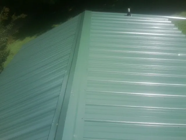 New green metal panels meeting at the ridge of a roof — Flat Roof Repair work by our crew in Ladoga
