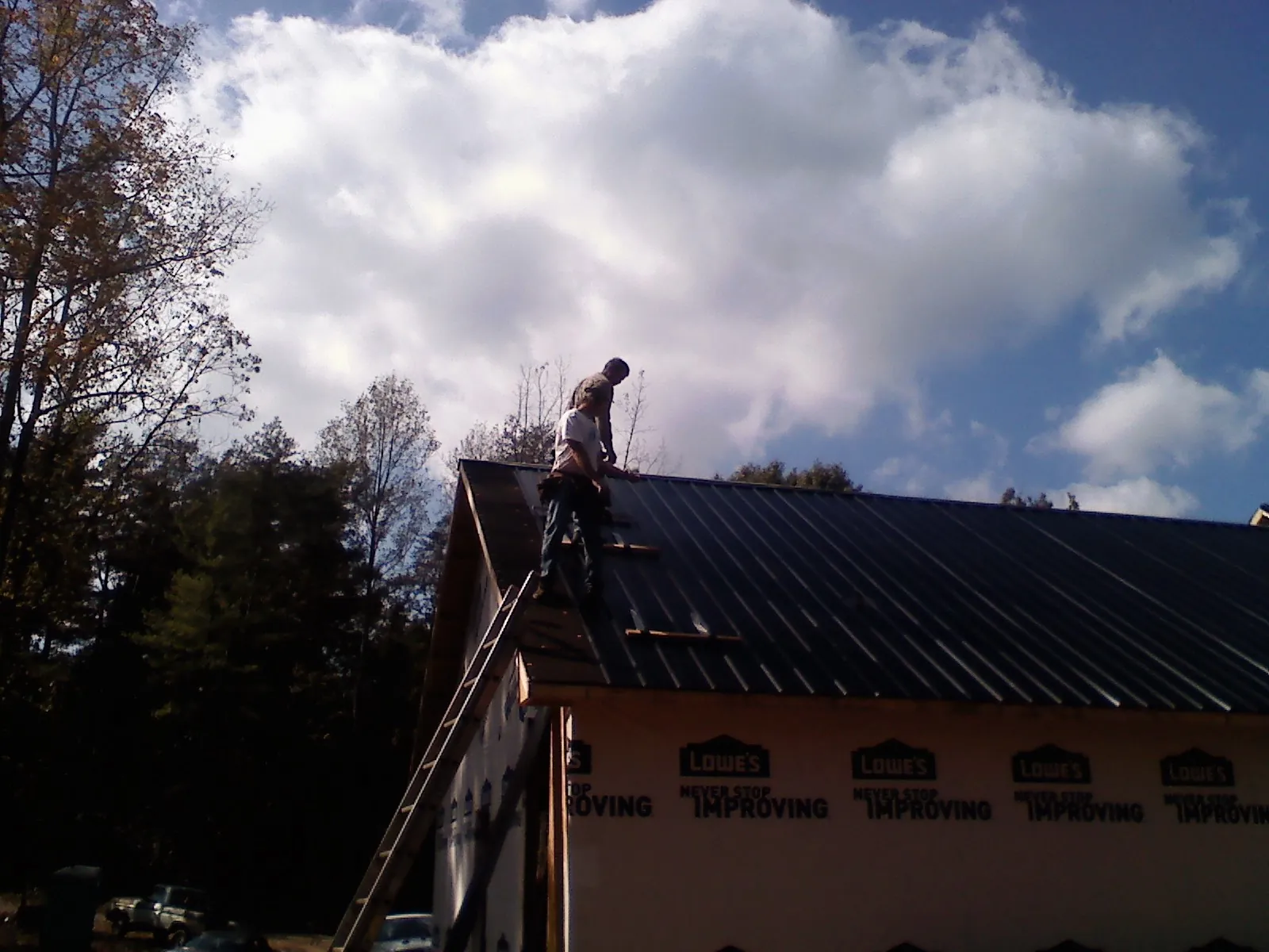 Roofer fastening dark metal panels high against a cloudy sky, from a Roof Inspection job in Ladoga