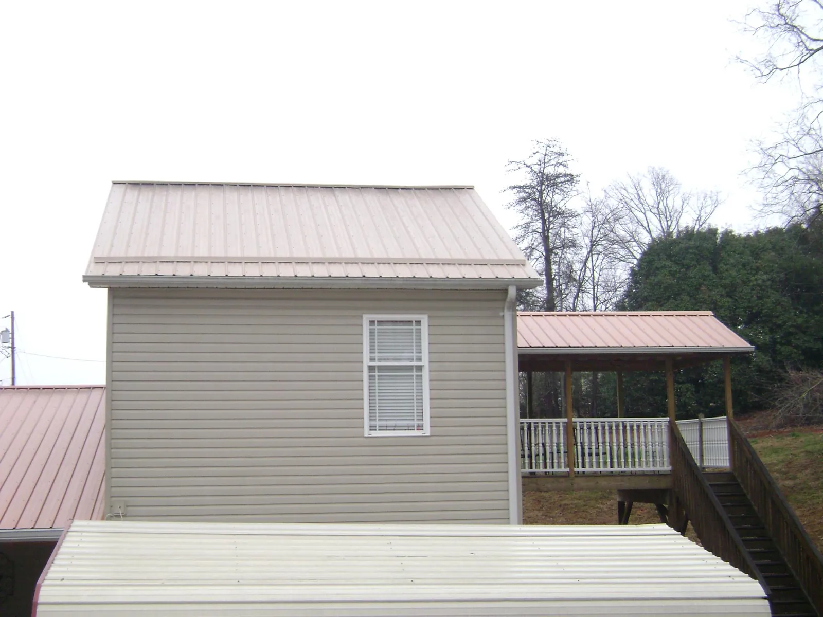Tan metal roofs on a two story addition and attached porch, from a Roof Replacement job in Ladoga